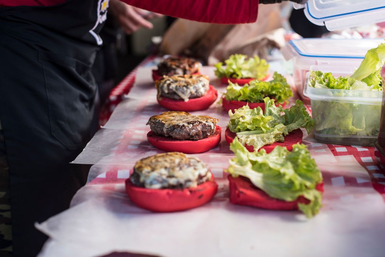 about-us Delicious gourmet burgers with unique red buns being prepared on a checkered table.
